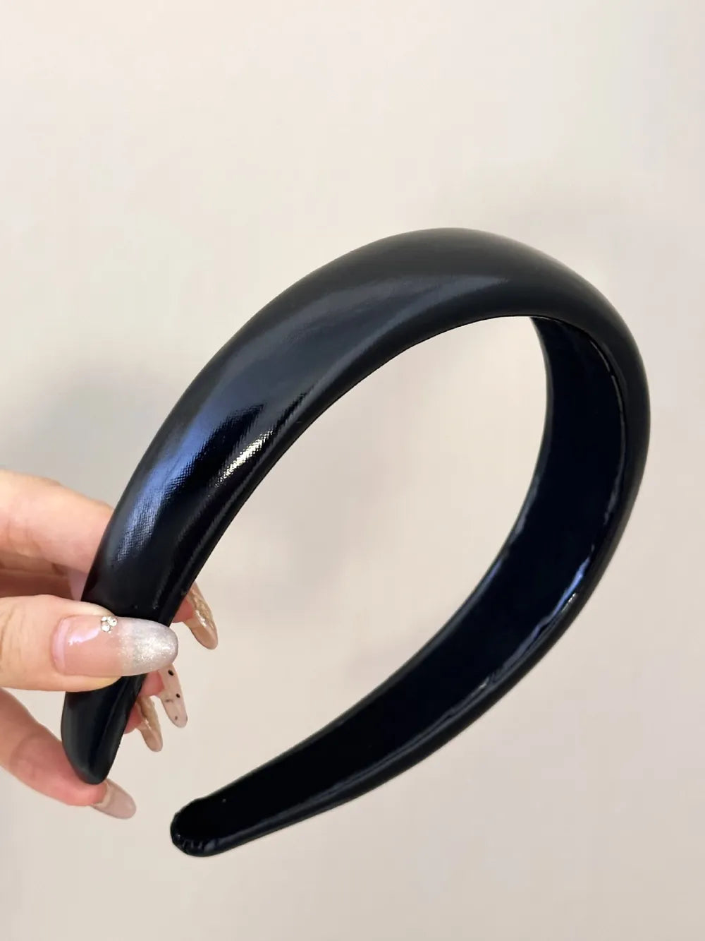 black PU leather wide headband with glossy finish held in hand

