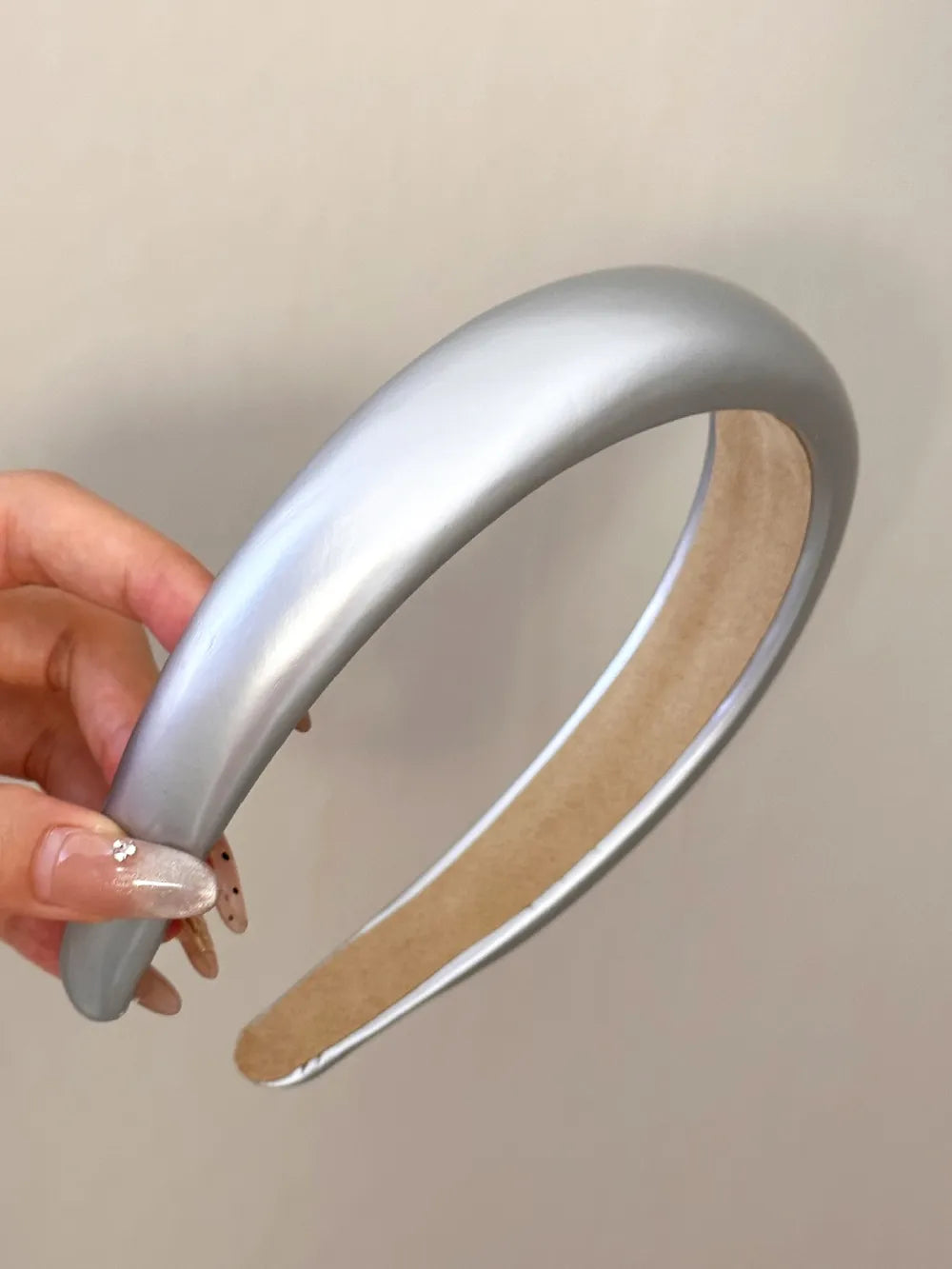 Silver headband held by a hand against a plain background