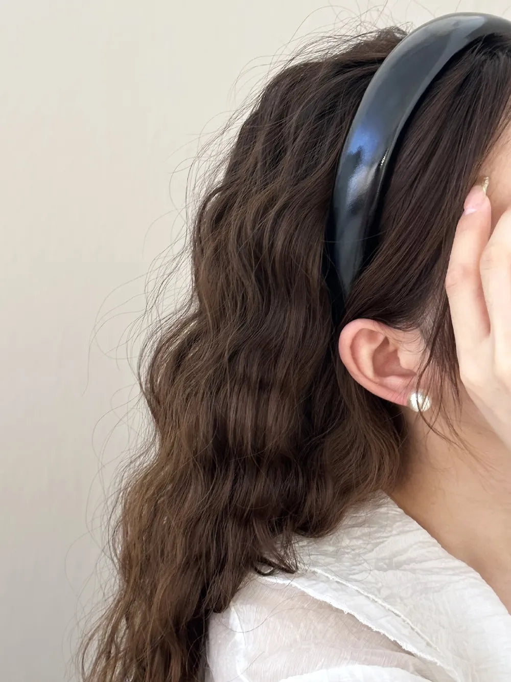woman styling black leather-look headband in long wavy hair
